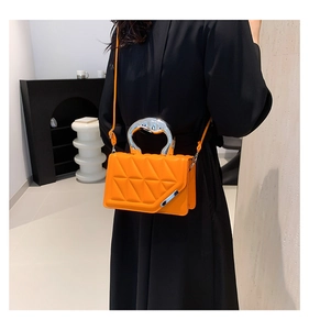Model wearing orange quilted handbag with silver handle and crossbody strap detail