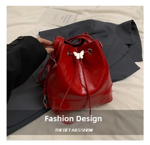 Detail of red patent leather bucket bag featuring white butterfly metal ornament and drawstring
