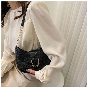 Detailed view of crocodile texture on black underarm bag with large pearl strap accents