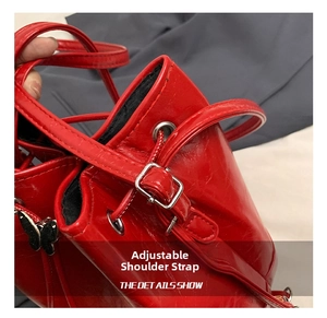 Detail of red glossy bucket bag with adjustable strap and silver butterfly charm