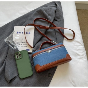 Detail of denim crossbody bag with brown leather trim and smartphone for size reference