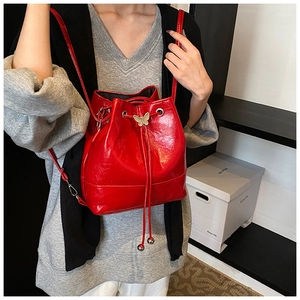 Detail of red glossy bucket bag featuring drawstring closure and gold butterfly ornament