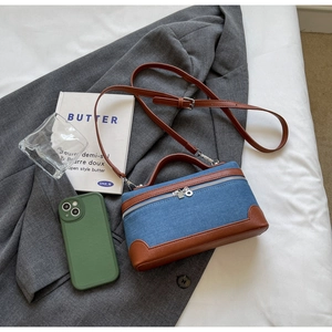 Detailed view of denim and brown leather contrast crossbody bag on a grey blazer