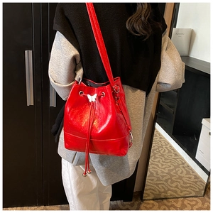 Side view of a bright red glossy bucket bag with silver butterfly charm on a model