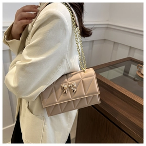 Dettaglio borsa a tracolla trapuntata beige con chiusura a fiocco dorato e catena metallica