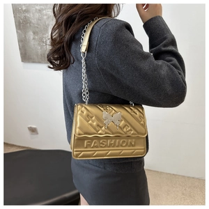 Détail d'un sac bandoulière doré en cuir PU avec texture matelassée et boucle papillon argentée