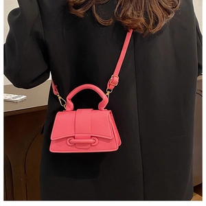 Close-up of bright pink lychee grain mini crossbody bag worn with a black blazer