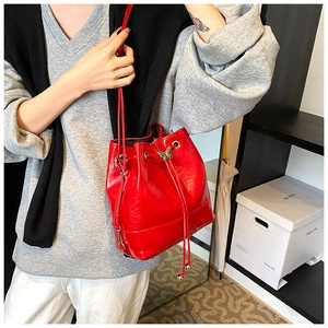 Detail of red patent leather bucket bag with metal butterfly buckle and drawstring