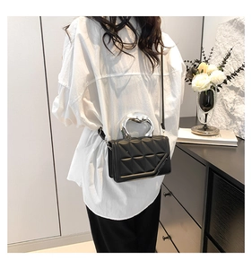 Detail of black quilted crossbody bag with liquid silver metal handle on model
