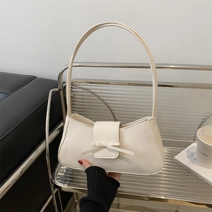 Creamy white leather baguette bag with bow detail on a modern minimalist indoor set