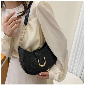 Macro detail of black crocodile pattern leather bag with gold buckle and pearl strap