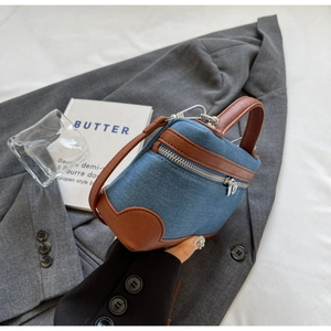 Close-up of denim and brown leather contrast Boston bag held against a grey suit jacket