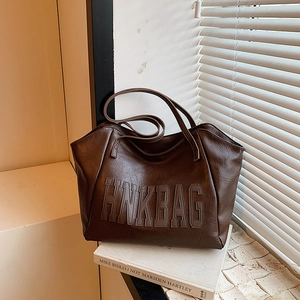 Brown faux leather tote bag with letter embossing shown in striped light and shadow