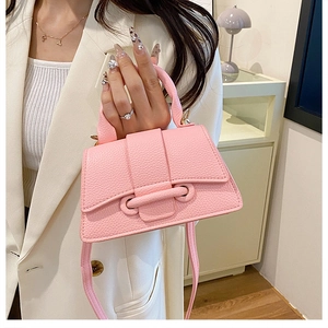 Detail of pink mini crossbody bag with litchi grain texture and top handle on beige blazer
