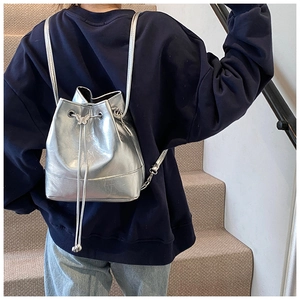 Silver metallic drawstring bucket bag with butterfly buckle detail worn by a model