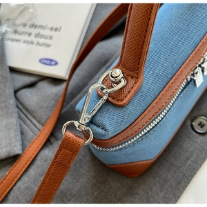 Detail of blue denim handbag with brown leather trim and silver metal hardware accents