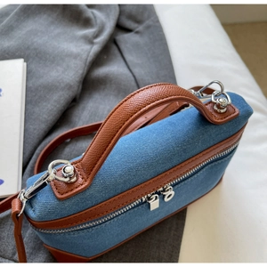 Detail of blue denim box bag with brown leather trim and silver metal zipper hardware