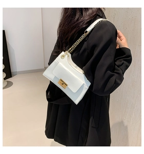 Detail of white square shoulder bag with gold metal lock and chain strap on model