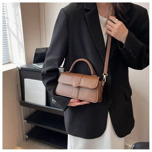 Close-up of brown matte leather handbag with golden hardware worn with a black blazer