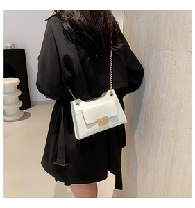 Detailed view of white leather crossbody bag with gold chain strap and square buckle
