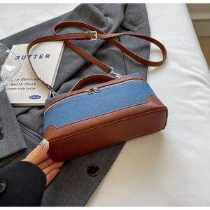 Detail view of denim and brown leather contrast crossbody bag on a minimalist backdrop