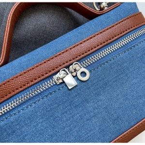 Detailed close-up of blue denim handbag featuring brown leather trim and dual silver zippers