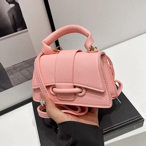 Pink lychee texture crossbody bag with top handle and gold hardware on a white desk