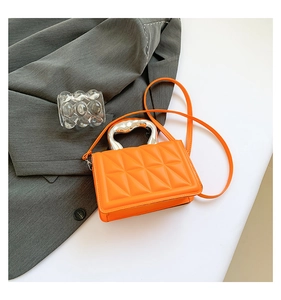 Detail of orange quilted handbag with unique silver handle on grey blazer backdrop