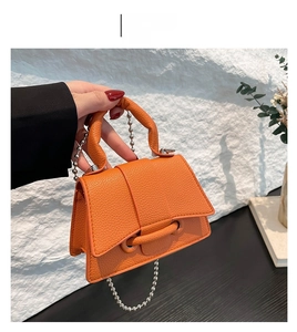Gros plan d'un sac à main orange en cuir grainé avec chaîne à billes et poignée haute