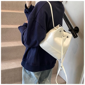 Close-up of a white drawstring bucket bag made from glossy faux leather with silver hardware
