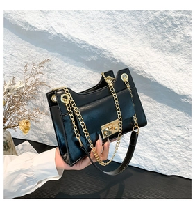Detail of black glossy leather handbag with gold chain strap and metallic twist lock