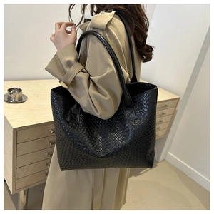 Detail of black woven texture tote bag worn with beige trench coat for office commute