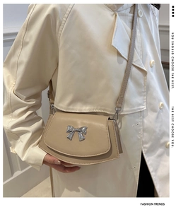 Close-up of a beige crossbody bag with a silver bow clasp worn over a beige trench coat