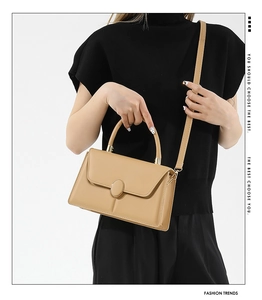 Detail of beige rectangular handbag with circular buckle shown on a model's shoulder