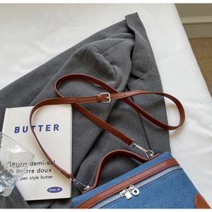 Detail view of denim crossbody bag with brown leather trim on a grey blazer background