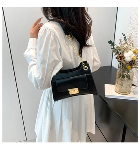Detail of a black leather shoulder bag with gold chain strap on a model and interior background