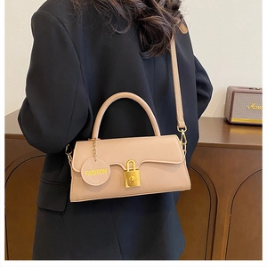 Detail of a beige leather crossbody bag with golden lock and fashion tag on a black coat