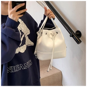 Detail view of white drawstring bucket bag with silver butterfly charm and PU leather texture