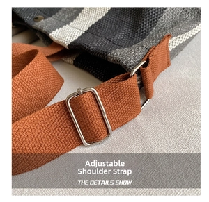 Detail of adjustable brown canvas strap with silver metal buckle on striped tote bag