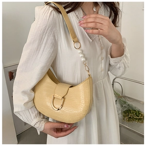 Detailed view of cream crocodile textured crescent bag with pearl strap on a white dress