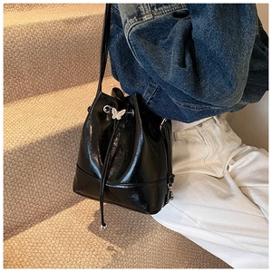 Detail of a black glossy bucket bag with silver butterfly hardware and drawstring
