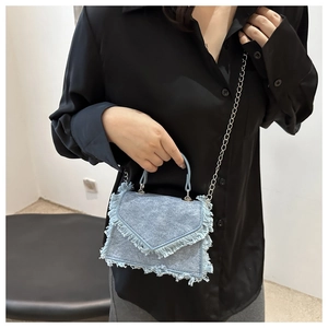 Detail of light blue denim mini crossbody bag with fringe edges and V-shaped flap