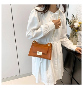 Detail of elegant brown leather bag with golden chain strap on a white dress model