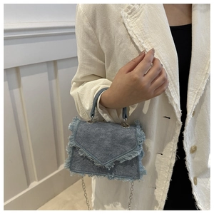 Detail of light blue denim mini bag showing fringe edges and silver chain strap