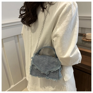 Detail of light blue denim handbag featuring distressed frayed edges and silver chain strap