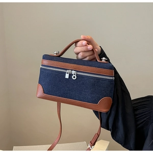 Detail of denim crossbody bag featuring brown leather trim and silver dual zippers