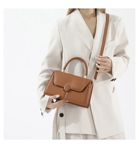 Close-up of caramel brown textured handbag with round metal buckle on white suit