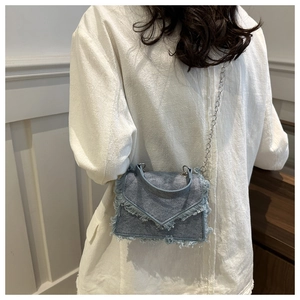 Close-up of light blue denim crossbody bag with frayed edges and silver metal chain