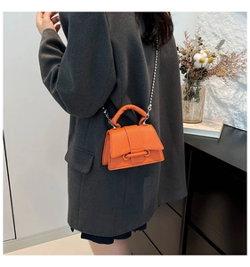 Mini sac orange en cuir grainé avec bandoulière chaîne porté sur un blazer gris