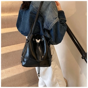 Detail view of black glossy bucket bag with silver butterfly buckle on a model